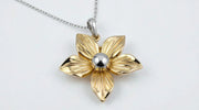 Close-up of a gold-plated flower-shaped pendant with a silver-tone center, hanging on a silver chain against a white background.