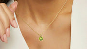 Close-up of a woman wearing a gold chain necklace with a round-cut green peridot pendant, gently holding the chain with manicured fingers.