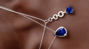 Elegant silver necklace featuring deep blue teardrop-shaped gemstones and delicate chain links, displayed on a smooth brown fabric background.