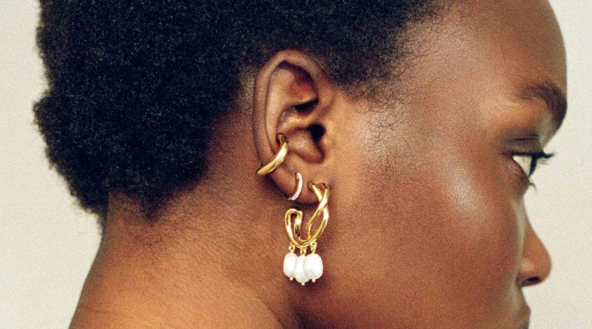 Close-up of a woman's ear adorned with multiple gold ear cuffs and a statement earring featuring three white dangling beads.