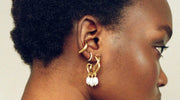 Close-up of a woman's ear adorned with multiple gold ear cuffs and a statement earring featuring three white dangling beads.