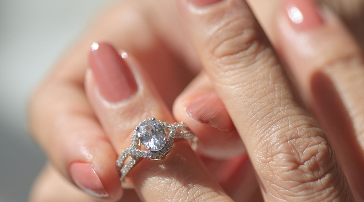Close-up of a woman's hand wearing a sparkling silver engagement ring with a large round-cut gemstone and twisted band design, featuring neatly manicured pink nails.