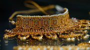 Close-up of an intricately designed traditional gold choker necklace adorned with pearls and gemstone details, displayed on a reflective surface.