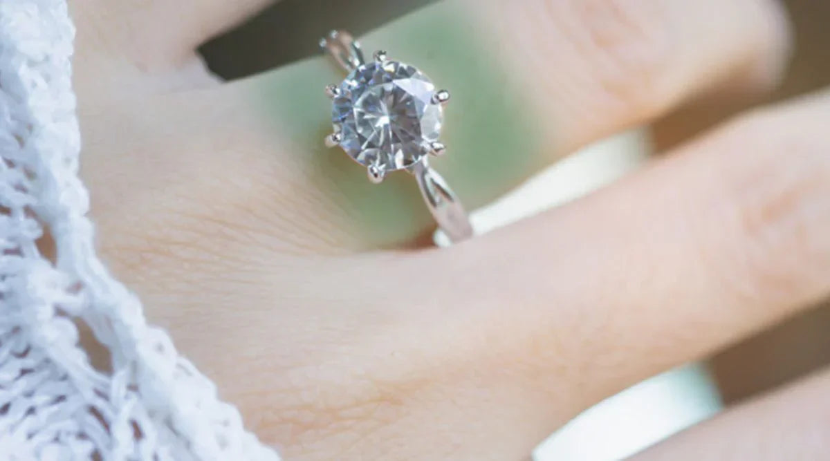 Close-up of a hand wearing a silver ring with a large round gemstone, showing a green stain on the skin beneath the ring.