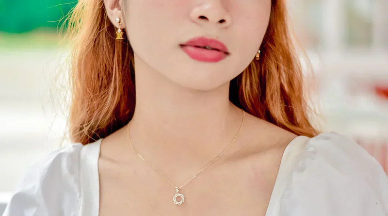 Close-up of a woman wearing a delicate gold necklace with a circular pendant and matching gold earrings, showcasing a standard necklace length around the collarbone.