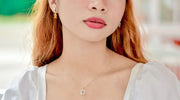 Close-up of a woman wearing a delicate gold necklace with a circular pendant and matching gold earrings, showcasing a standard necklace length around the collarbone.