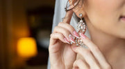 Close-up of a bride wearing elegant, sparkling chandelier earrings, with soft pink manicured nails gently adjusting the earring.