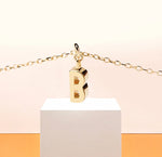 Dainty gold initial "B" necklace on anchor chain, reflecting soft elegance and personal charm.
