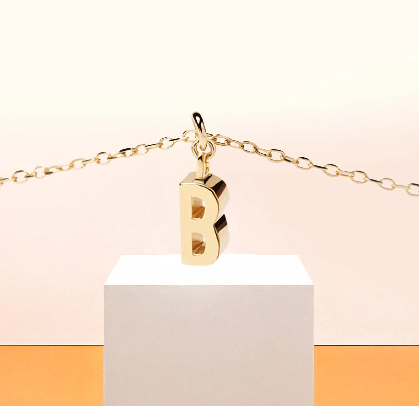 Dainty gold initial "B" necklace on anchor chain, reflecting soft elegance and personal charm.