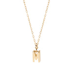 Petite gold initial M pendant hanging from an anchor chain, designed for subtle shimmer and perfect for layering with other delicate pieces.
