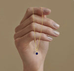 Elegant birthstone jewelry featuring a vivid blue sapphire, suspended on a delicate gold chain designed for layering or solo wear.
