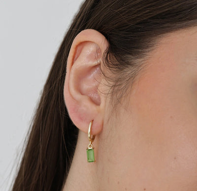 Elegant dangling hoop earrings with vibrant peridot baguette stones suspended from dainty gold hoops.
