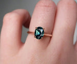 Oval teal sapphire engagement ring with sparkling diamond halo for a unique proposal ring
